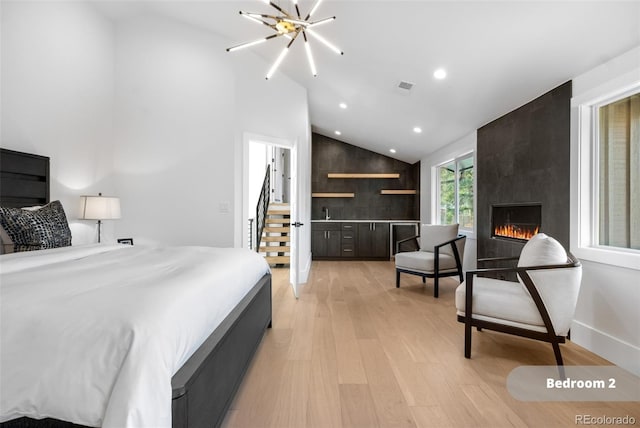 bedroom featuring lofted ceiling, a large fireplace, light hardwood / wood-style floors, and a chandelier