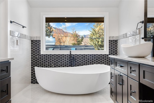 bathroom with a washtub, vanity, tile patterned floors, and tile walls