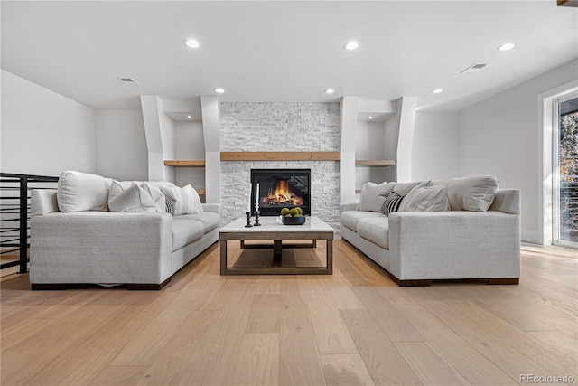 living room with built in shelves, a stone fireplace, and light hardwood / wood-style flooring