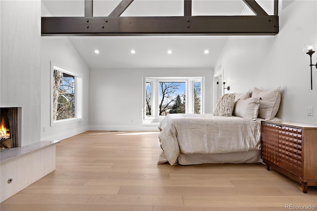 bedroom with lofted ceiling with beams, a large fireplace, and light hardwood / wood-style flooring