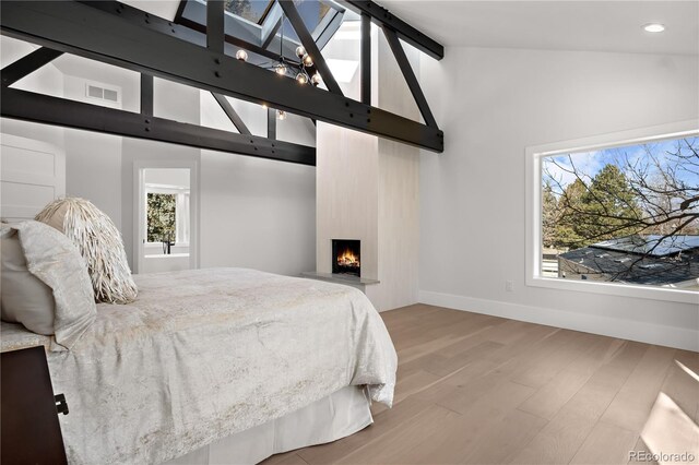 bedroom with hardwood / wood-style floors, lofted ceiling with beams, and a large fireplace