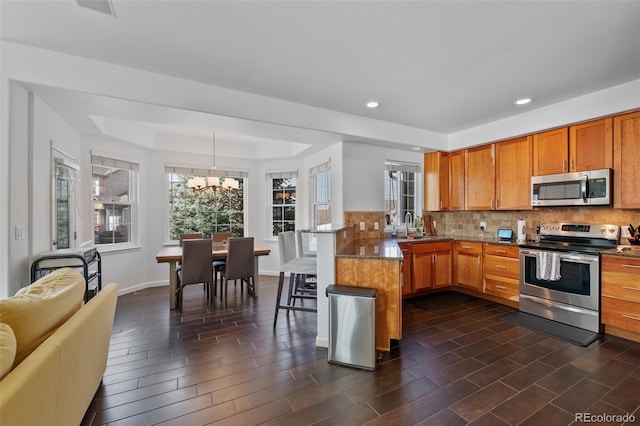 kitchen with a notable chandelier, kitchen peninsula, sink, hanging light fixtures, and stainless steel appliances