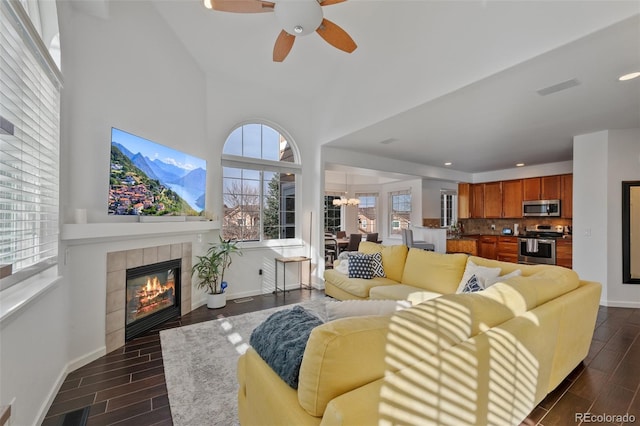 living room with ceiling fan with notable chandelier and a tiled fireplace