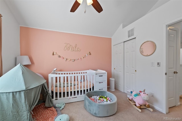 carpeted bedroom with ceiling fan, a nursery area, a closet, and vaulted ceiling