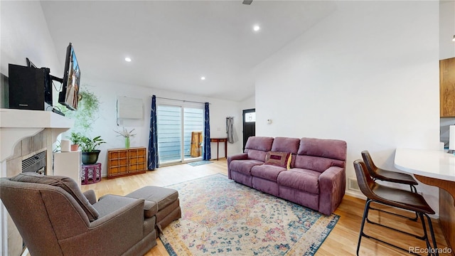 living room with light wood-type flooring, recessed lighting, a tiled fireplace, and vaulted ceiling