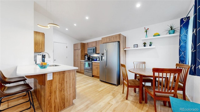 kitchen featuring brown cabinets, a sink, a peninsula, light wood-style floors, and stainless steel appliances