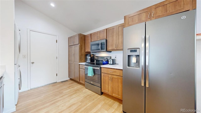 kitchen with light wood finished floors, light countertops, washer / clothes dryer, stainless steel appliances, and vaulted ceiling