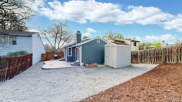 rear view of property with an outdoor structure, a patio, a fenced backyard, a chimney, and a storage unit