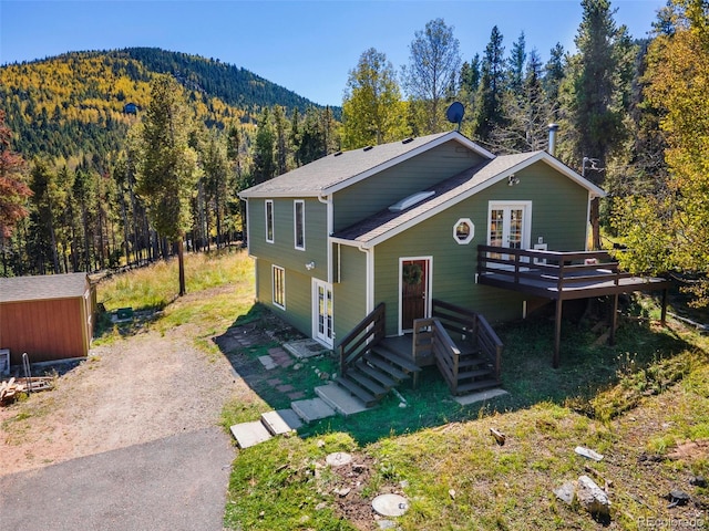 32252 Steven Way, Conifer, CO 80433 - view of front facade featuring a view of trees, a deck with mountain view, driveway, french doors, and a shingled roof