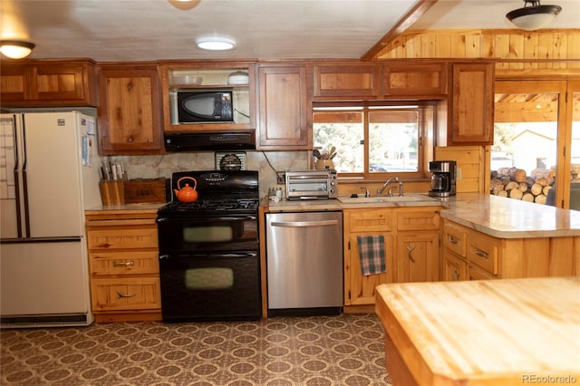 kitchen featuring range hood, a peninsula, a sink, black appliances, and tasteful backsplash