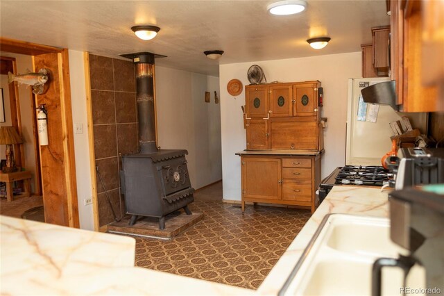 kitchen with light countertops, freestanding refrigerator, a wood stove, brown cabinetry, and a sink