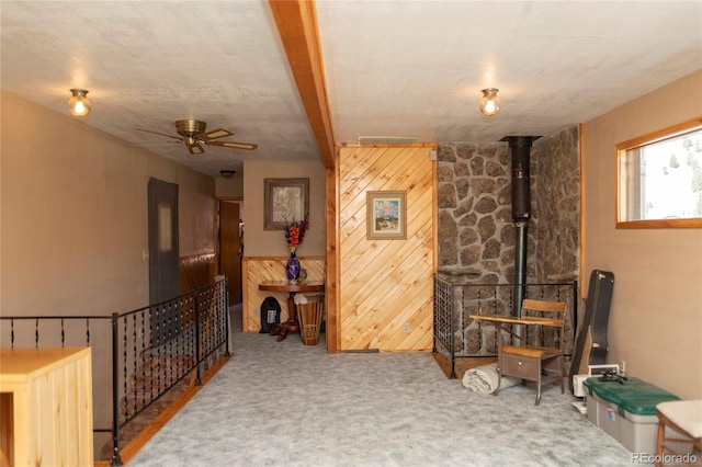 interior space with wooden walls, carpet flooring, a wood stove, and ceiling fan