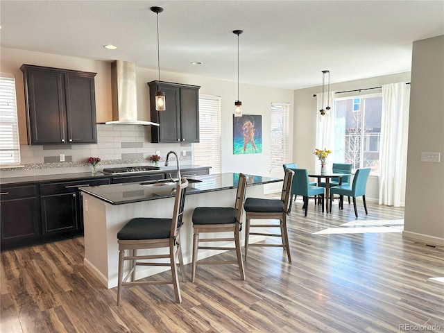 9482 Kendrick Way, Arvada, CO 80007 - kitchen with wall chimney range hood, a sink, dark countertops, a kitchen breakfast bar, and dark wood-style floors