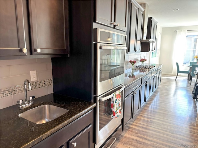 9482 Kendrick Way, Arvada, CO 80007 - kitchen with stainless steel double oven, tasteful backsplash, dark brown cabinets, dark stone counters, and light wood finished floors
