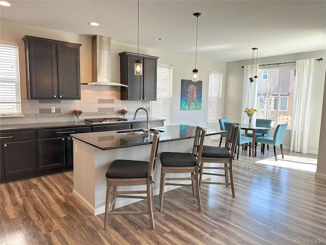 9482 Kendrick Way, Arvada, CO 80007 - kitchen with wall chimney range hood, dark countertops, stainless steel gas stovetop, a kitchen breakfast bar, and dark wood-type flooring