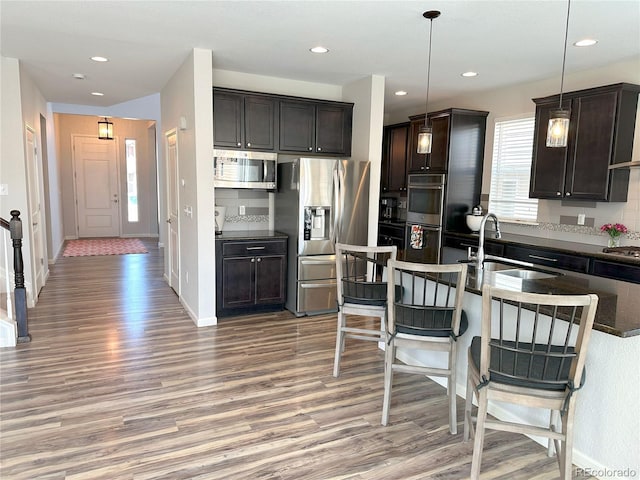 9482 Kendrick Way, Arvada, CO 80007 - kitchen featuring stainless steel appliances, light wood-type flooring, a breakfast bar, dark brown cabinets, and recessed lighting