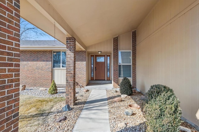 doorway to property featuring brick siding and roof with shingles