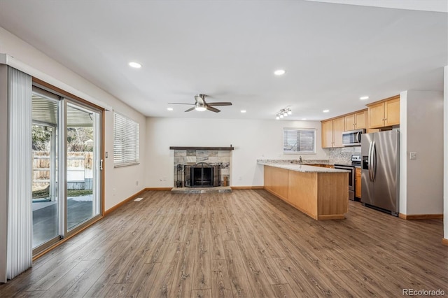 kitchen featuring stainless steel appliances, a stone fireplace, a peninsula, and wood finished floors