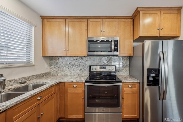 kitchen featuring tasteful backsplash, brown cabinetry, appliances with stainless steel finishes, light stone counters, and a sink