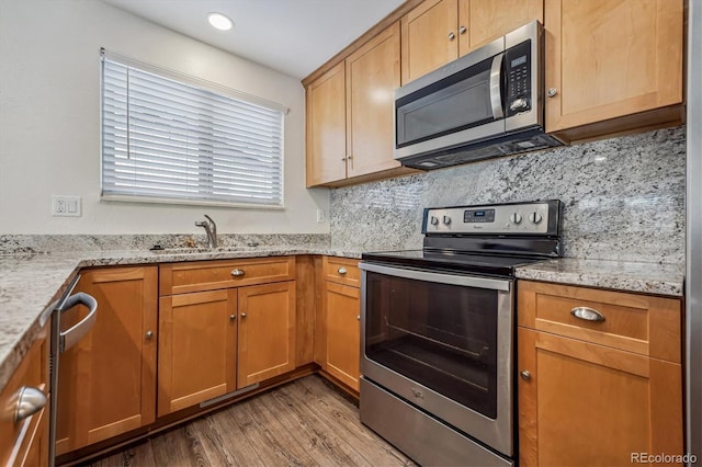 kitchen with light stone counters, tasteful backsplash, light wood-style flooring, appliances with stainless steel finishes, and a sink