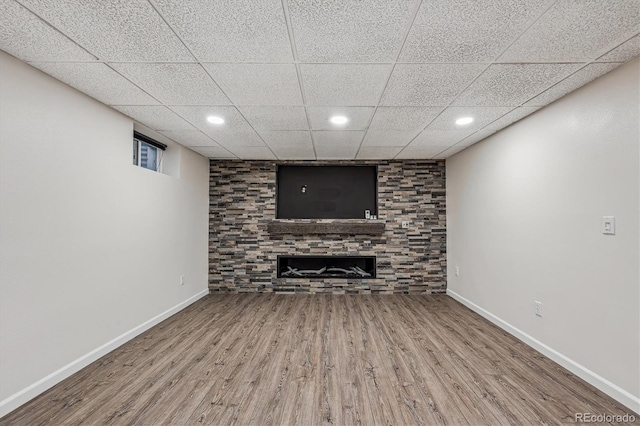 finished basement featuring baseboards, a drop ceiling, a tiled fireplace, and wood finished floors