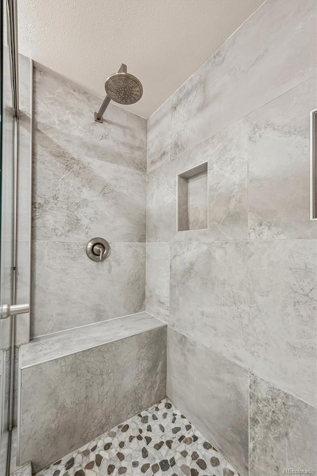 bathroom with a tile shower and a textured ceiling