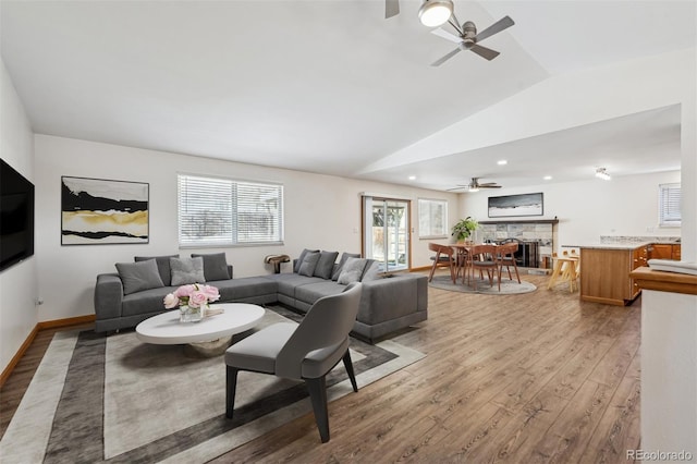 living area with lofted ceiling, a fireplace, a ceiling fan, baseboards, and light wood-style floors