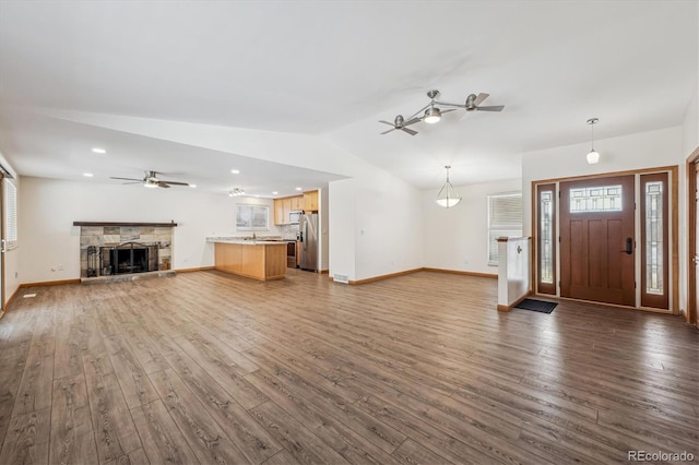 unfurnished living room with a ceiling fan, wood finished floors, vaulted ceiling, a fireplace, and a wealth of natural light