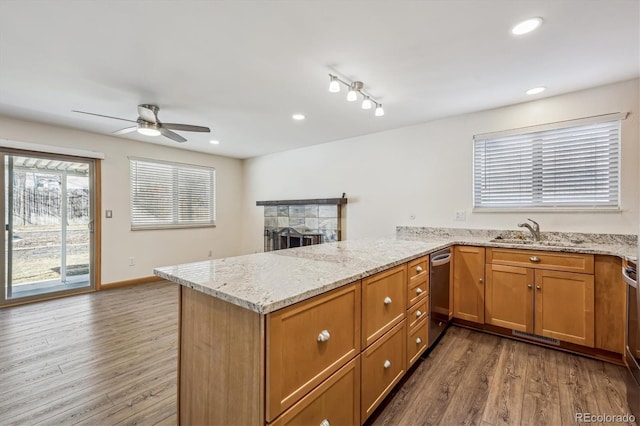 kitchen featuring a stone fireplace, recessed lighting, a peninsula, wood finished floors, and light stone countertops