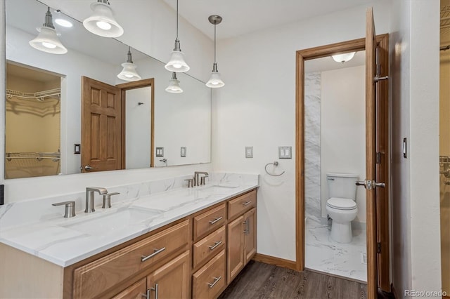 full bath featuring double vanity, toilet, a sink, and wood finished floors