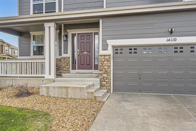 entrance to property featuring covered porch, an attached garage, and stone siding
