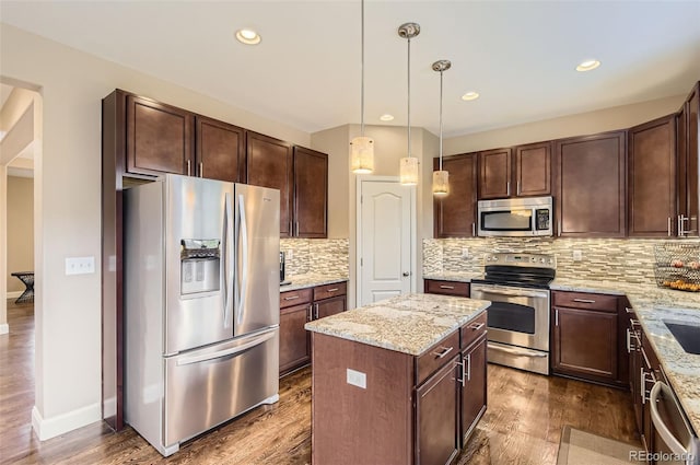 kitchen featuring dark brown cabinets, a center island, tasteful backsplash, light stone counters, and appliances with stainless steel finishes
