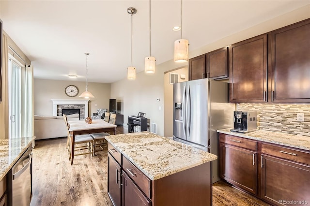 kitchen featuring a stone fireplace, tasteful backsplash, wood finished floors, open floor plan, and stainless steel appliances