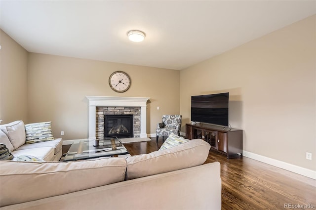 living room featuring dark wood-style flooring, baseboards, and a stone fireplace