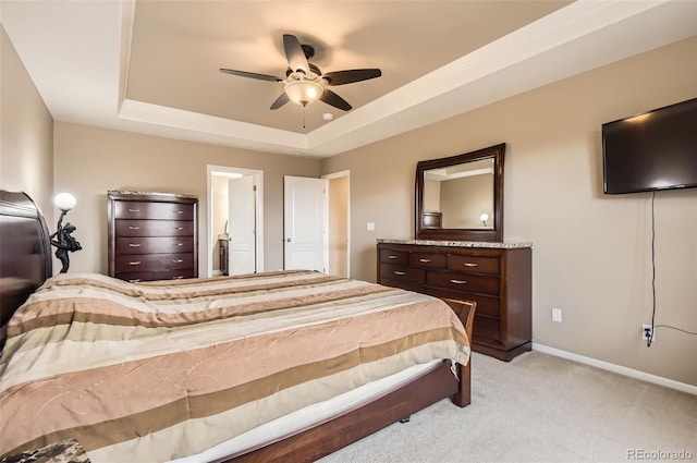 bedroom featuring a ceiling fan, light colored carpet, baseboards, ensuite bathroom, and a tray ceiling