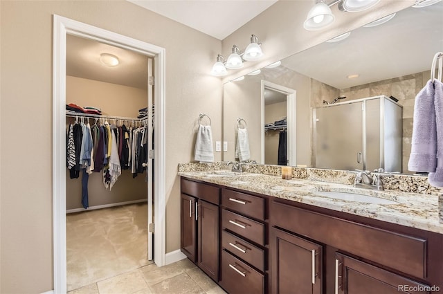 bathroom featuring double vanity, a sink, a stall shower, and a spacious closet