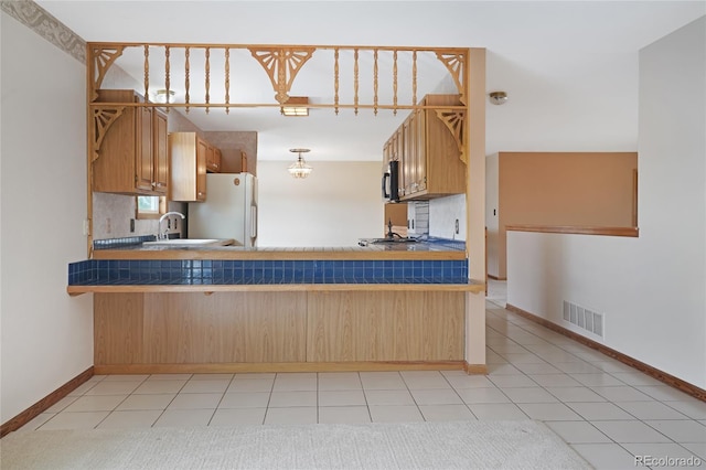 kitchen featuring a sink, visible vents, freestanding refrigerator, and a peninsula