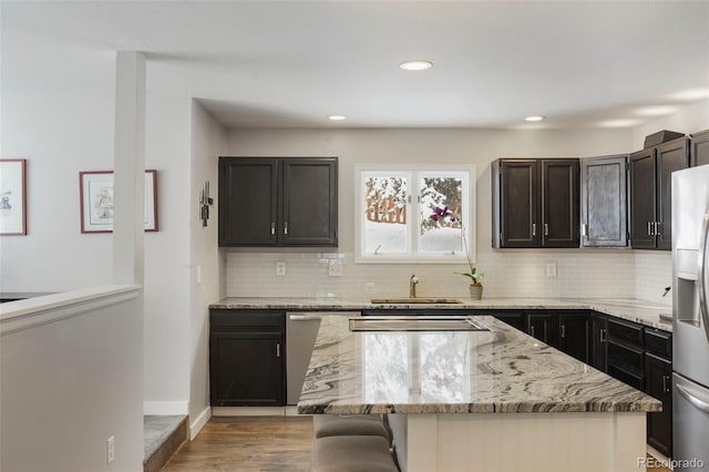 kitchen with light stone countertops, a breakfast bar, stainless steel appliances, sink, and light hardwood / wood-style floors