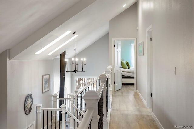 hallway featuring a notable chandelier, a skylight, high vaulted ceiling, and light hardwood / wood-style flooring