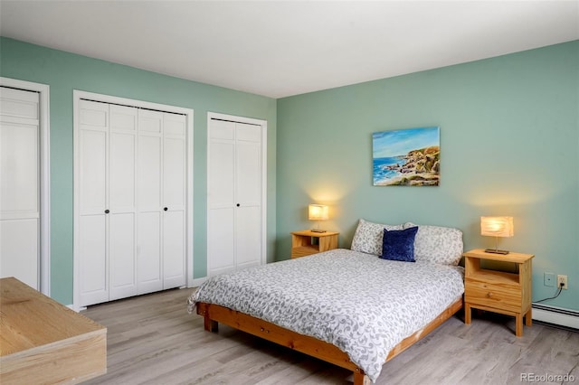 bedroom featuring baseboard heating, two closets, and light wood-type flooring