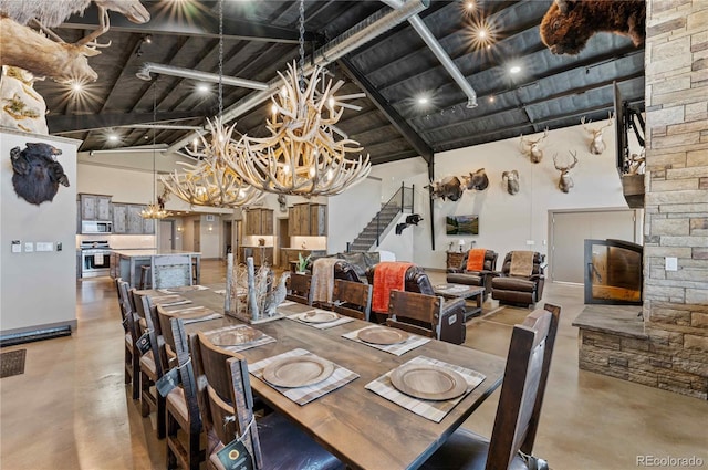 dining space featuring high vaulted ceiling, beamed ceiling, a notable chandelier, concrete floors, and a fireplace