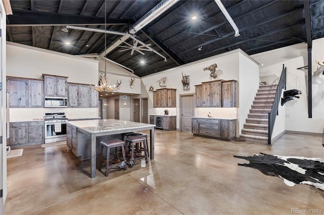 kitchen featuring a spacious island, appliances with stainless steel finishes, concrete floors, decorative light fixtures, and a breakfast bar area