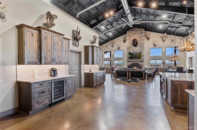 kitchen featuring light stone counters, beverage cooler, decorative light fixtures, high vaulted ceiling, and a fireplace