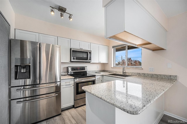 kitchen featuring sink, light hardwood / wood-style flooring, kitchen peninsula, white cabinets, and appliances with stainless steel finishes