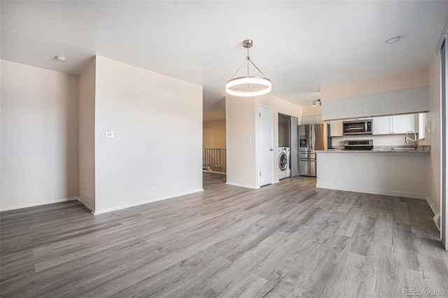 unfurnished living room featuring washer / dryer, light wood-type flooring, and sink