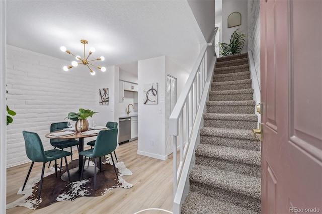 dining room featuring a chandelier, brick wall, light wood finished floors, and stairs