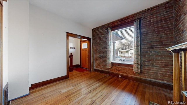 empty room with light hardwood / wood-style flooring, a wealth of natural light, and brick wall