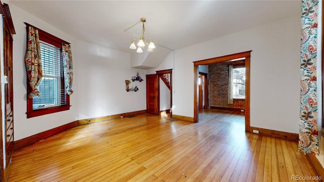 empty room featuring wood-type flooring, an inviting chandelier, a healthy amount of sunlight, and brick wall