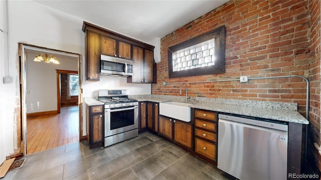 kitchen with light stone countertops, sink, dark hardwood / wood-style flooring, brick wall, and appliances with stainless steel finishes