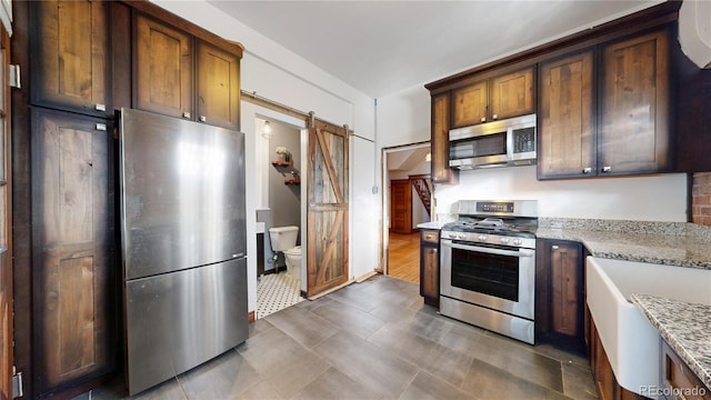 kitchen with a barn door, light stone counters, dark hardwood / wood-style floors, and appliances with stainless steel finishes